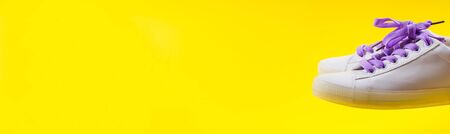 White sneakers with purple laces on yellow background. Modern minimal fashion art trendy bold color still lifeの写真素材