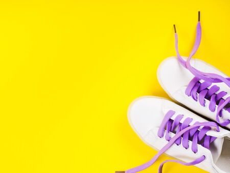 White sneakers with purple laces on yellow and purple split background. Modern minimal fashion art trendy bold color flat lay still lifeの写真素材