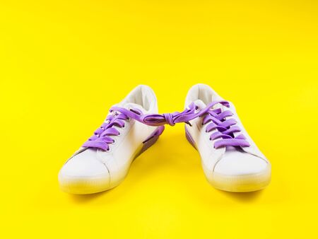 White sneakers with purple laces on yellow background. Modern minimal fashion art trendy bold color still lifeの写真素材