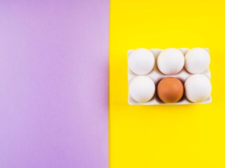 White and one brown egg on yellow and purple split duotone background. Easter, art food creative conceptの写真素材