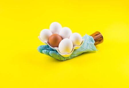 White eggs in palm of wooden hand wearing blue medical glove on yellow bold color paper background....