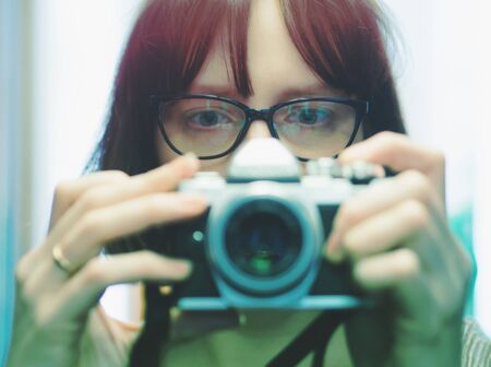Young girl wearing glasses making selfie on digital camera in front of the mirror. Self portrait