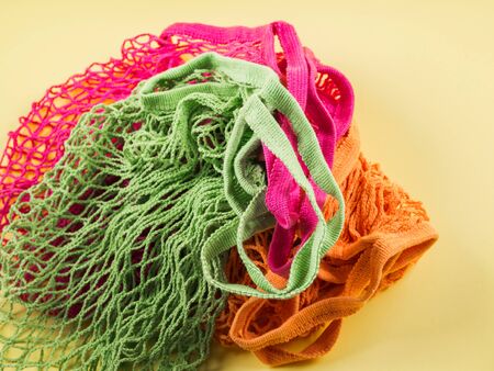 Colorful reusable shopping mesh bags on yellow background. Zero waste concept flat lay