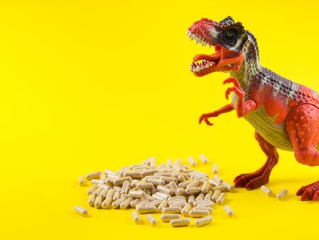 Maca powder in capsules on yellow background with funny toy dinosaur above the pills. Food supplement for energy boosting.の写真素材