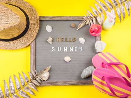 Hello summer text on letter board on yellow background with straw hat, flip flops, seashells and stones, golden tropical branches. Flat layの写真素材