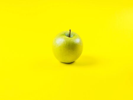 Shiny fresh green apple on bold yellow background. Healthy diet minimal concept. Vitamins