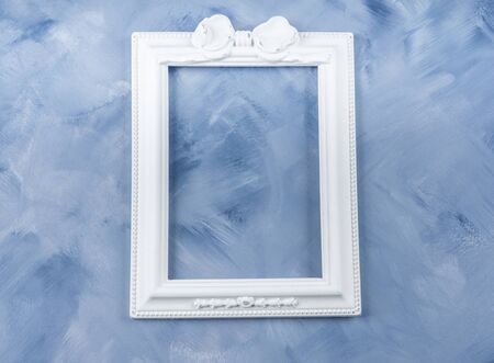 Empty white romantic picture frame on blue. Flat lay, top view. Festive background for textの写真素材