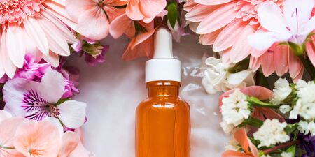 Skin care serum in orange bottle with dropper with beautiful flowers around. Natural beauty productの写真素材