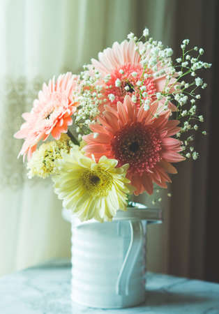 Yellow and pink gerbera daisy bouquet in white rustic watering can near a window. Verticalの写真素材