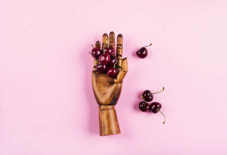 Heap of cherries in black wooden hand on pink background. Hello summer conceptの写真素材