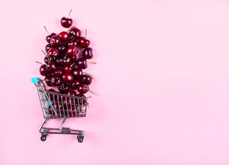 Cherries in toy shopping cart on pink background. Fresh summer produce. Flat lay, copy space