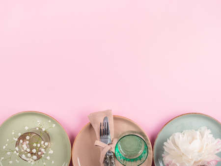 Pastel color crockery tableware with white flowers on pink background. Textured ceramic plates dishes, transparent glasses. Table setting conceptの写真素材