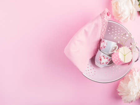 Pink colander with pink cups and napkin framed by peonies. Spring tableware conceptの写真素材