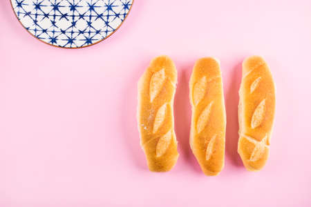 Three freshly baked mini baguette on pink background. Flat lay with empty dishの写真素材