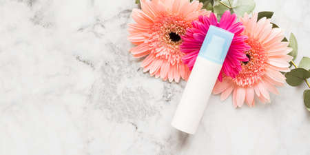Face moisturizer over pink flowers on marble. Beauty skin care products concept. Banner with copy...