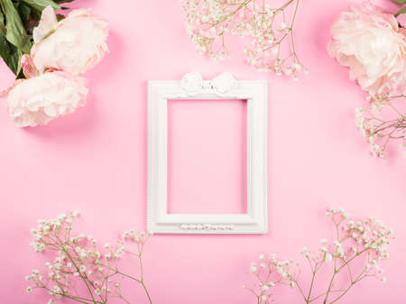 Pink pastel delicate invitation, greeting card background with floral decor with peonies. Flat lay mockup with white empty frameの写真素材