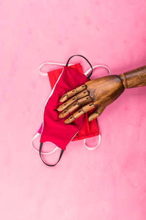 Hand made red face masks protection under black wooden hand on pink background. New normal fashion in times of Coronavirus Covid-19の写真素材