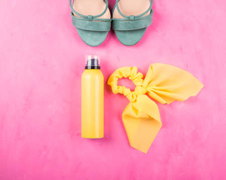 Yellow sun protection spray, hair tie with bow and female green sandals over pink background. Summer in the city or in vacation. Flat layの写真素材
