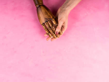 White female caucasian hand holds black wooden hand on pink wooden background. Joint support and assistance in the community.の写真素材