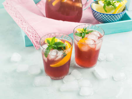 Fresh red cocktail mocktail sangria in pitcher and glasses with ice, mint leaves and lemon and orange slices on bright turquoise backgroundの写真素材