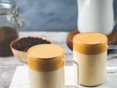 Whipped dalgona coffee drink in glass mug on white wooden board. Cozy breakfast with trendy beverage