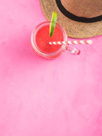 Straw hat and refreshing red watermelon smoothie on pink background. Summer relaxation, verticalの写真素材