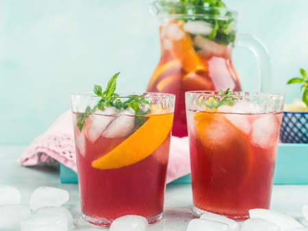 Fresh red cocktail mocktail sangria in pitcher and glasses with ice, mint leaves and lemon and orange slices on bright turquoise background. Closeupの写真素材