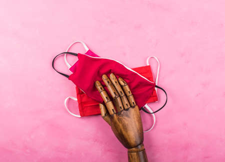 Hand made red face masks protection under black wooden hand on pink background. New normal fashion...