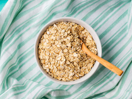 Gluten free oatmeal flakes in white bowl on green turquoise napkin background. Overhead closeup