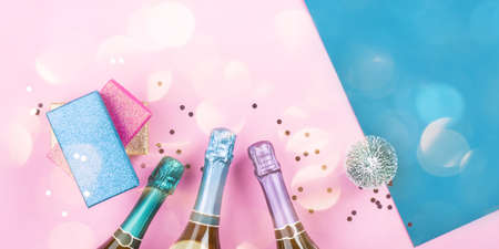 Champagne bottle, gifts and confetti on pink and blue background with sparkling confetti. Celebrating new year, christmas festive flat lay bannerの写真素材