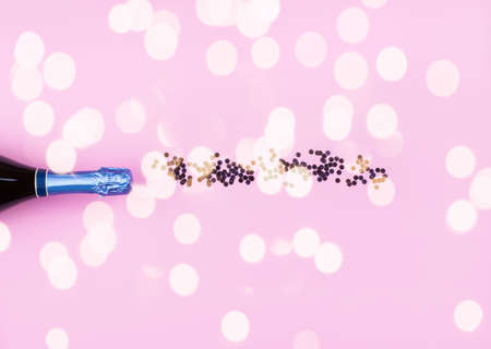 Champagne bottle with confetti as bubbles on pink color background. Celebrating concept festive flat...