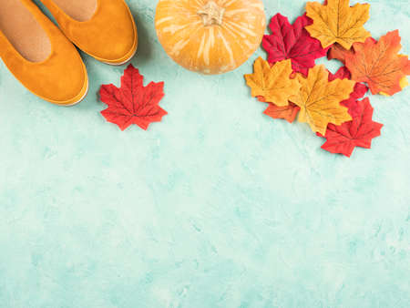 Female trendy yellow mustard flat shoes with autumn leaves and pumpkin, seasonal symbols over turquoise background. Flat lay, copy spaceの写真素材