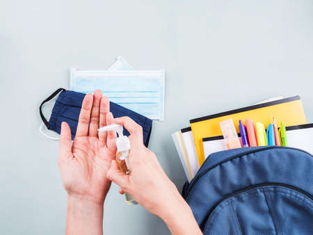 New school set after Covid quarantine including backpack with stationery, books and protective face masks, sanitizer. Hands applying sanitiser gelの写真素材