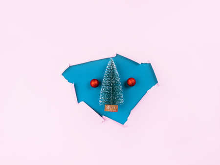 Toy christmas tree with red ornament in AI Aqua paper hole on pink background. Festive winter flat lay.の写真素材