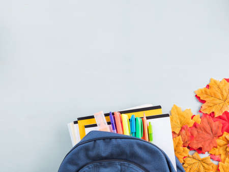 Back to school concept with blue backpack with stationery, copybooks, autumn leaves