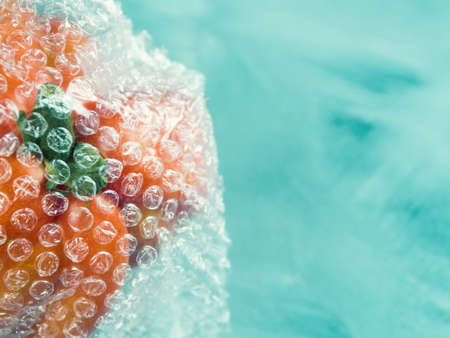 Tomato in plastic package on turquoise background. Plastic invasion concept, macro shot