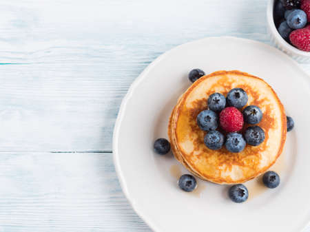Stack of pancakes with fresh blueberries served in a dish with maple syrup. Delicious breakfast top view on white wooden table.の写真素材