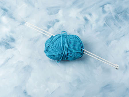 Blue wool knitting yarn with needles on faded background. Copy space