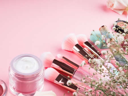 Shiny make up products and accessories on pink background with flowers. Trendy holographic brushes.の写真素材