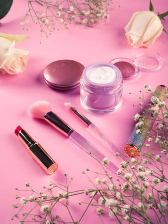 Shiny make up products and accessories on pink background with flowers. Trendy holographic brushes.の写真素材