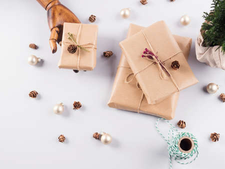 Christmas gifts wrapped in craft paper, pine cones and minimal festive ornament in wooden hand. Flat...