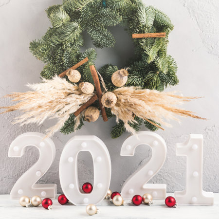 New 2021 year numbers lights with festive xmas red decor, spruce wreath on gray wall and white...