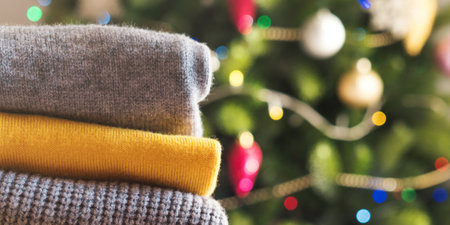 Yellow illuminated color and gray winter sweaters stack on decorated christmas tree background. Trendy fashion autumn warm cozy clothes as gift or holiday outfit conceptの写真素材