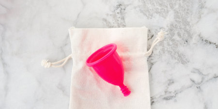 Pink menstrual cup on its storage cotton bag on marble table. Zero waste concept for female hygiene products. Bannerの写真素材