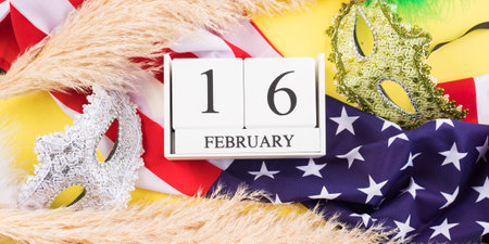 2021 Mardi Gras masks on american flag, February, 16 date on wooden calendar and pampas grass on yellow background. Bannerの写真素材