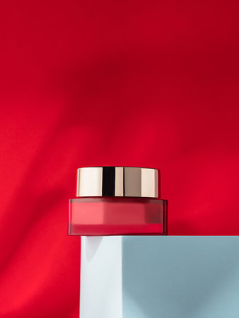 Beauty cream jar with metallic lid on blue podium red background with shadows. Skin care conceptの写真素材