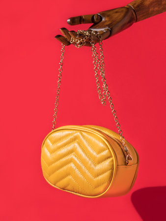 Wooden hand holding yellow eco leather bag on red background. Female fashion accessoriesの写真素材