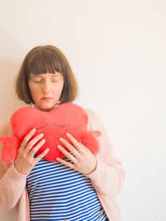 Young woman wearing striped t-shirt hugging red heart shaped plush toyの写真素材
