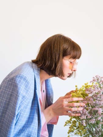 Young woman wearing blue jacket and pink shirt holding beautiful dried flowers bouquet on light gray...