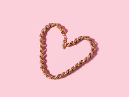 Trendy valentines day backgound with golden necklace heart and hard shadow on pinkの写真素材